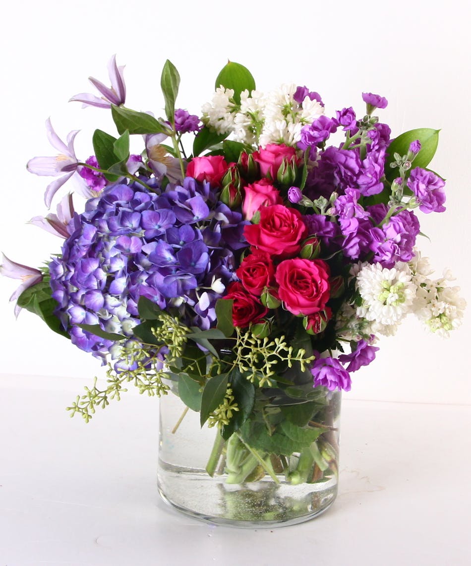 Lilacs, hydragnea, stock and spray roses in a clear glass vase