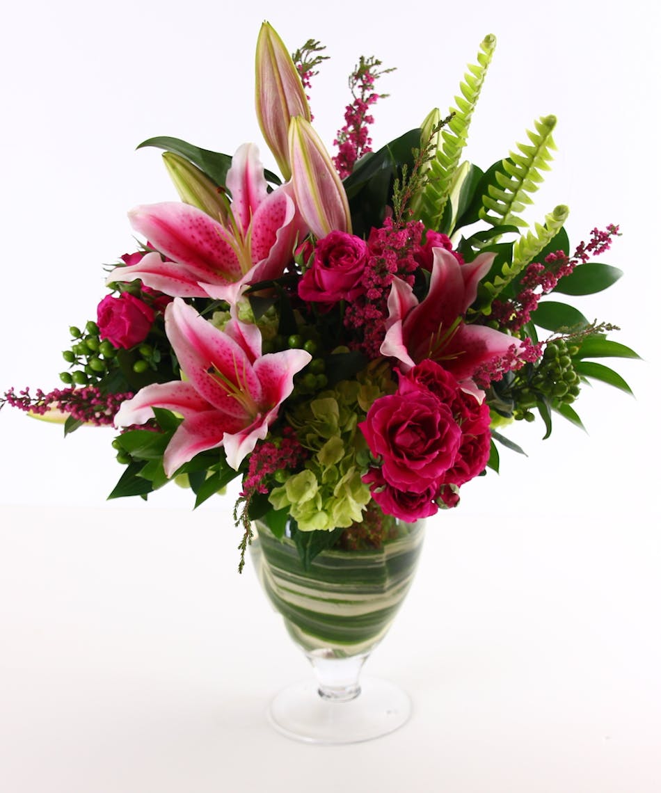 Lilies, roses, and hydrangea in a leaf lined glass vase.